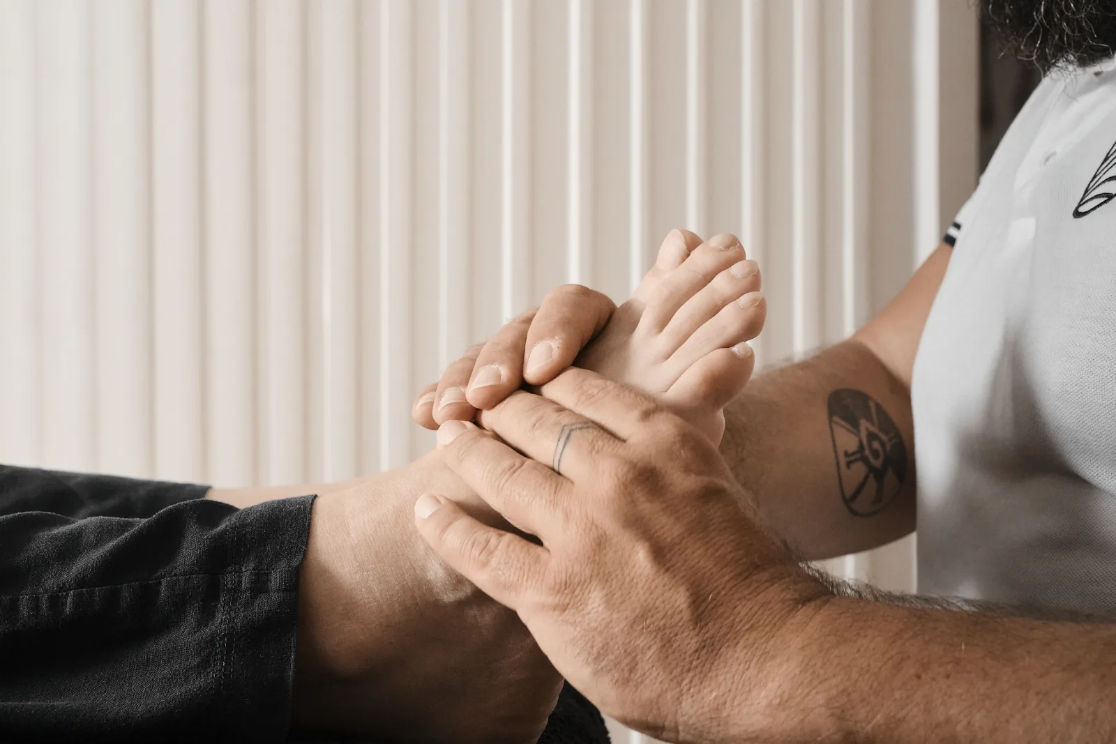 Due mani che avvolgono completamente un piede, la persona distesa su un telo scuro